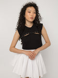 Model wearing Girl Code black pierced cutout crop top with a white pleated skirt