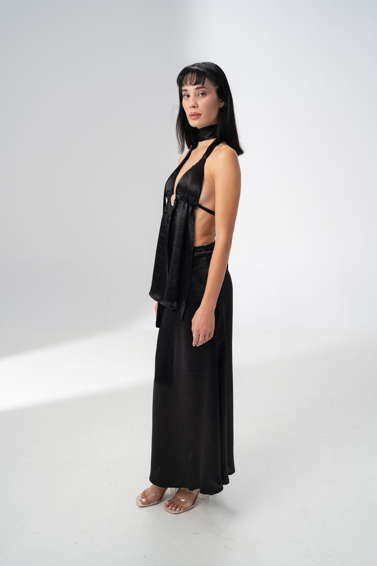 Deep V neckline of the black satin halter top gathered by a statement metal ring