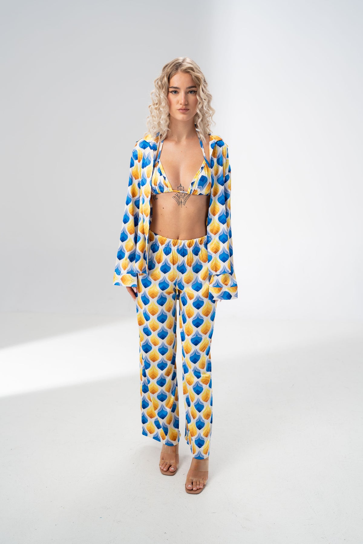 Model wearing the Girl Code blue and yellow satin three piece set with bralette, wide leg trousers and open shirt