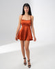 Model wearing the Girl Code burnt orange satin backless dress with fine straps and a ruffled skirt