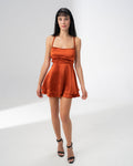 Model wearing the Girl Code burnt orange satin backless dress with fine straps and a ruffled skirt