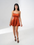Model wearing the Girl Code burnt orange satin backless dress with fine straps and a ruffled skirt