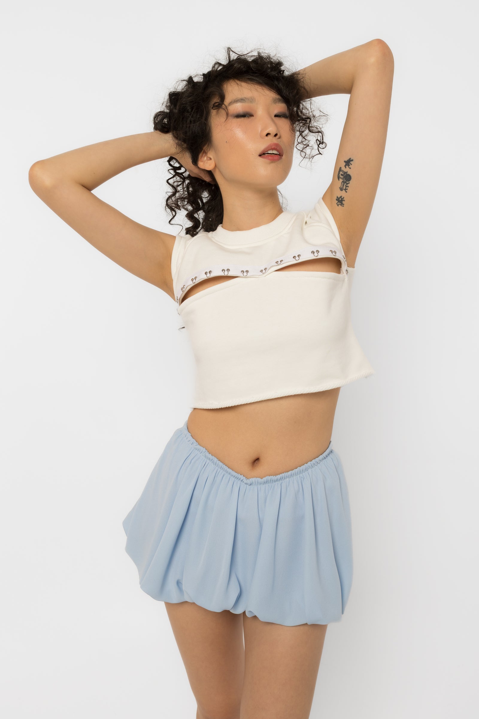 Model wearing Girl Code white pierced cutout crop top with steel rings