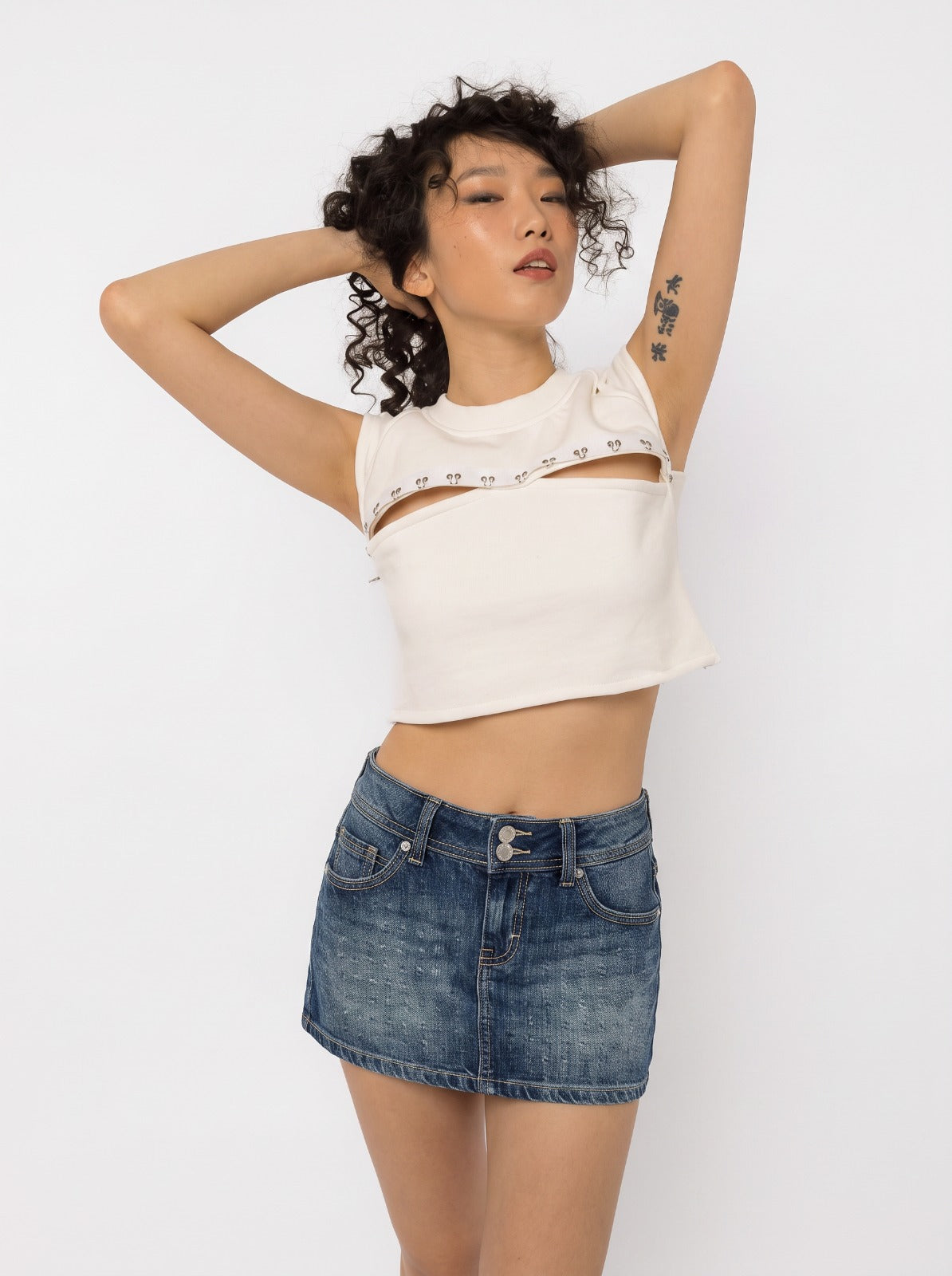 Model wearing Girl Code white pierced cutout crop top with steel rings, three quarter view